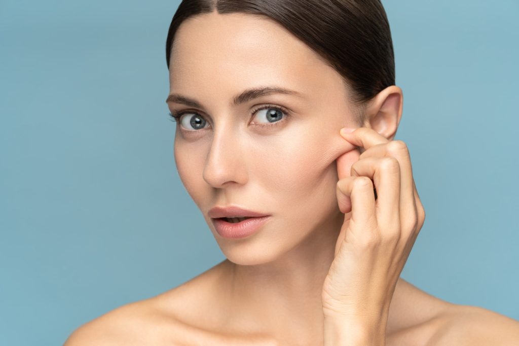 Woman without makeup touching cheeks after glycolic acid peel, has signs of aging skin on her face